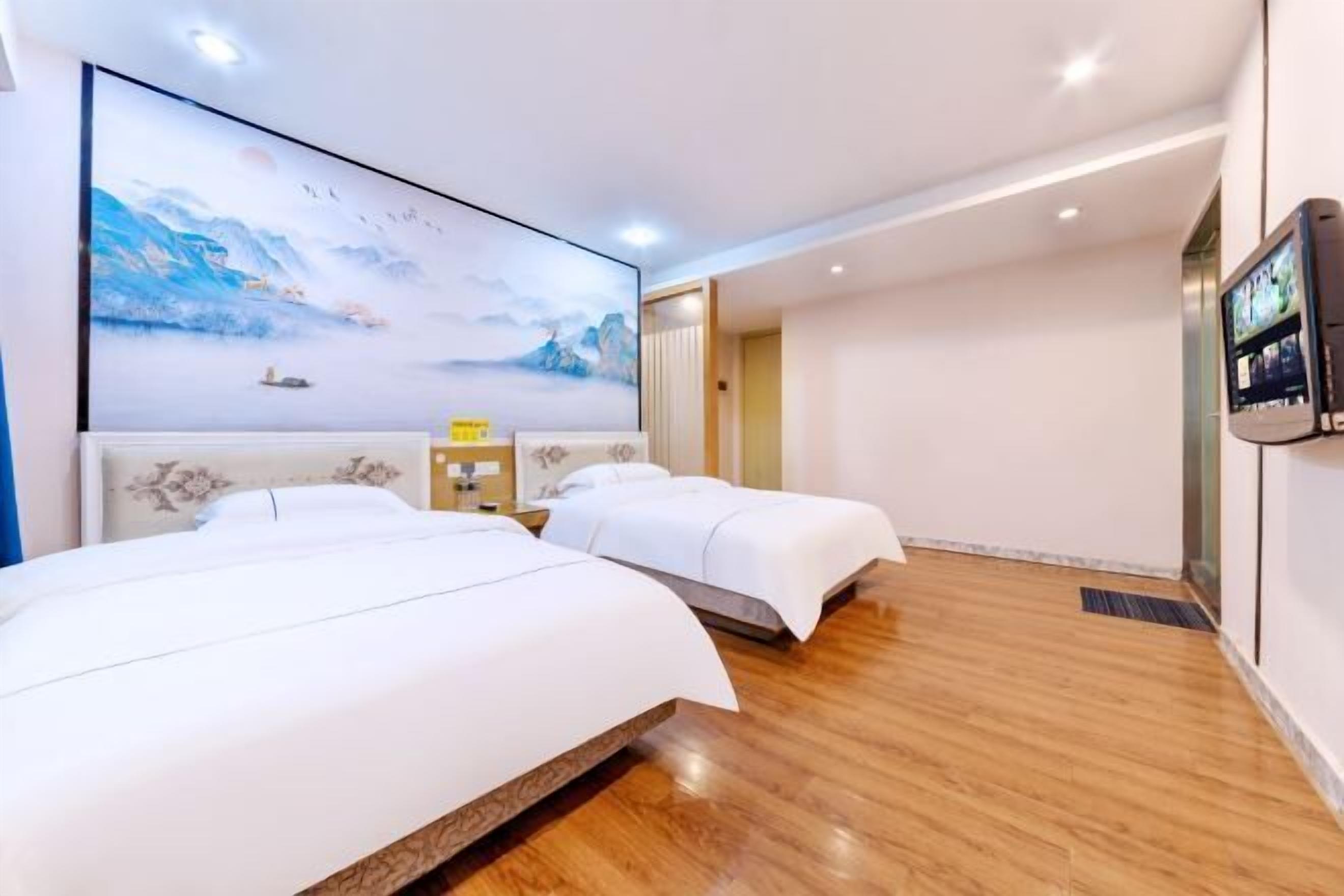 Quarto de hotel com duas camas, uma televisão grande montada na parede e piso de madeira.