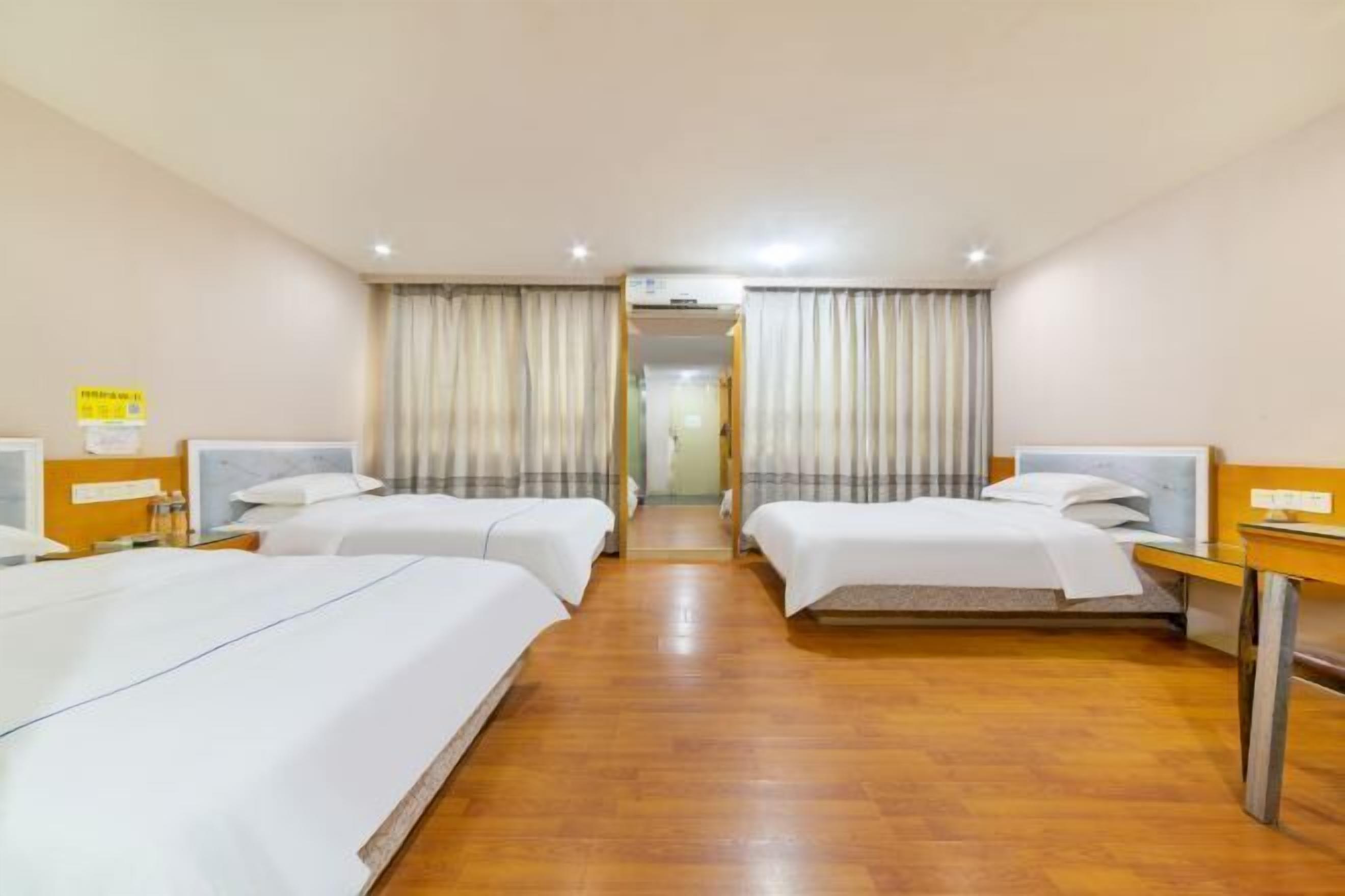 Quarto de hotel com duas camas, piso de madeira e corredor que leva a outro quarto.