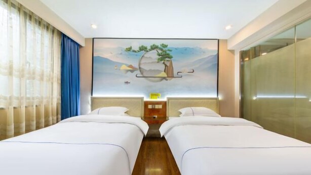 Hotelkamer met twee bedden, een houten vloer, een schilderij van een boom aan de muur en een nachtkastje met een lamp.
