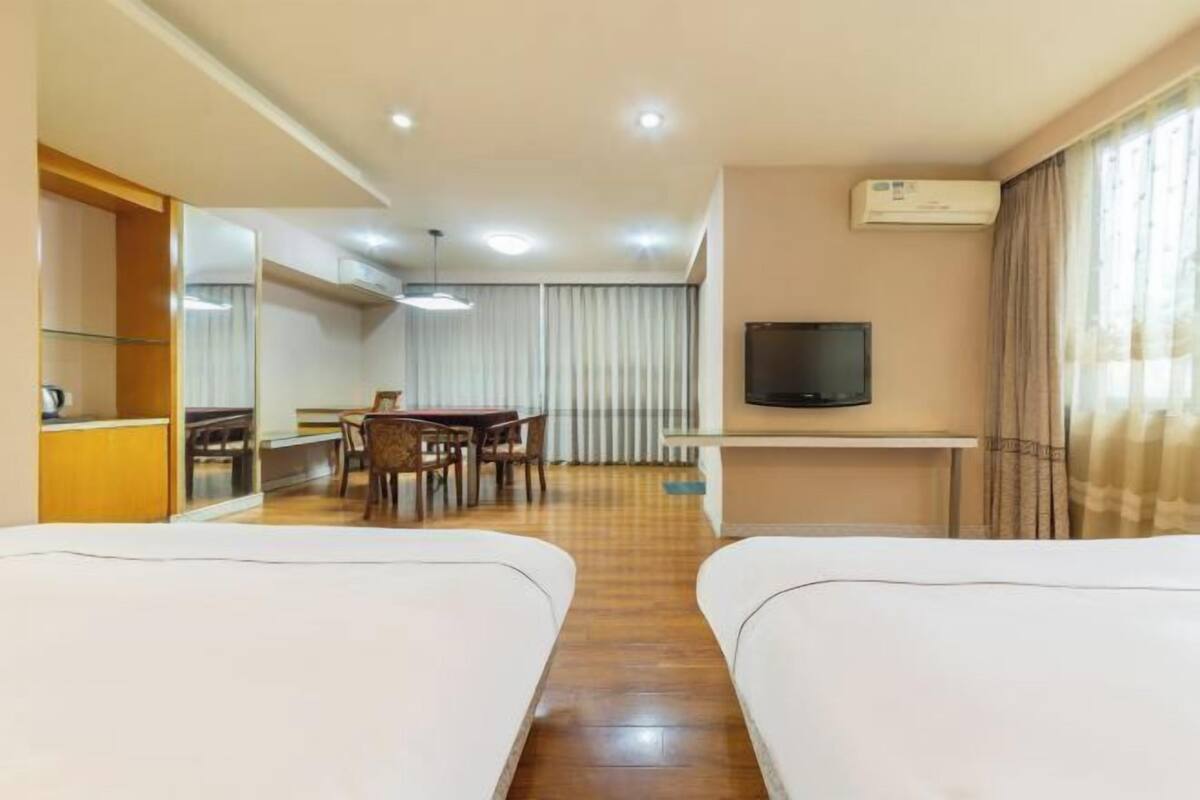 Een hotelkamer met twee bedden, een eettafel met stoelen, een televisie en een airconditioning.