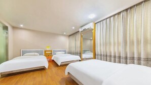 Een hotelkamer met drie bedden, een houten vloer, een spiegel en een raam met gordijnen.