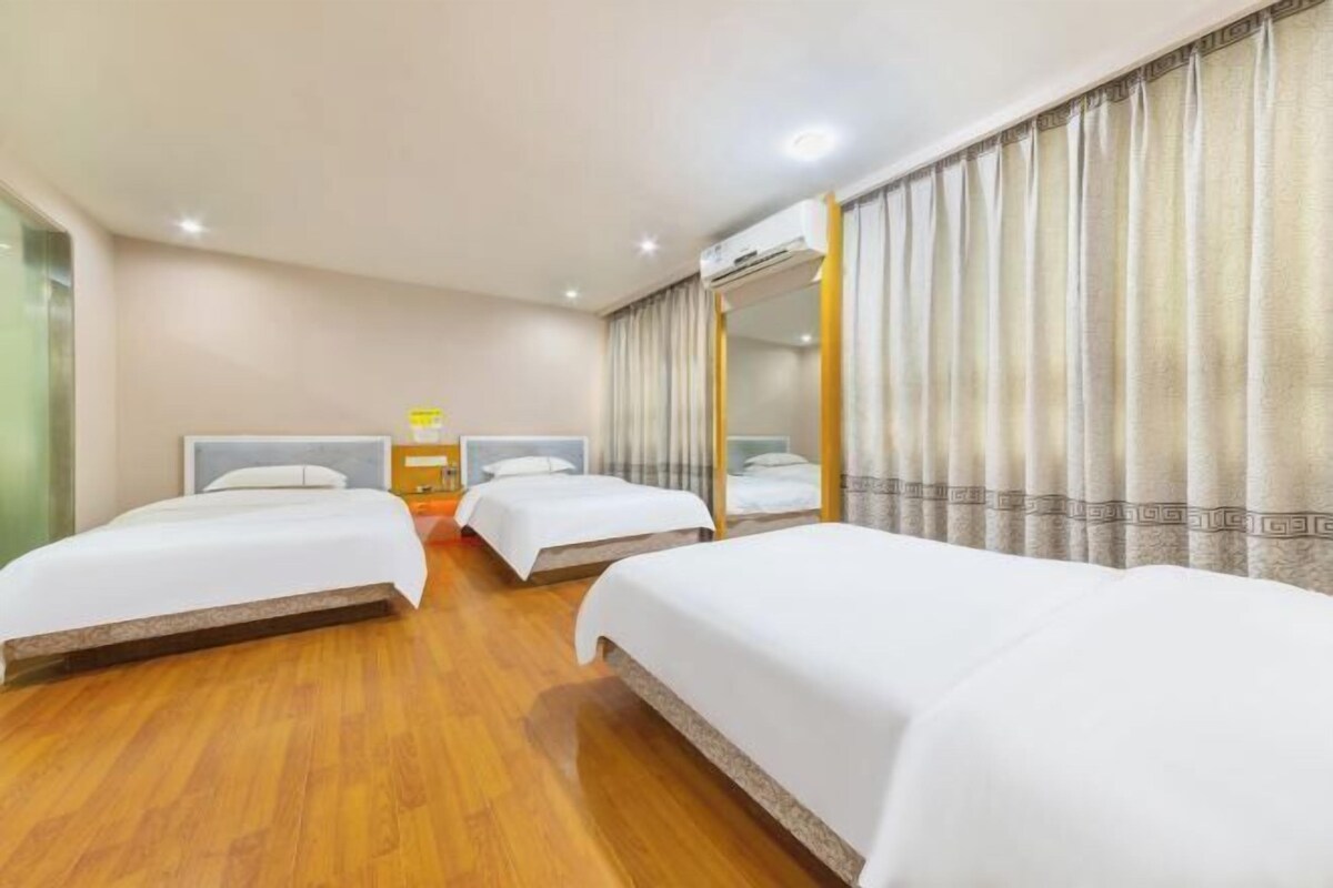 A hotel room with three beds, a wooden floor, a mirror, and a window with curtains.