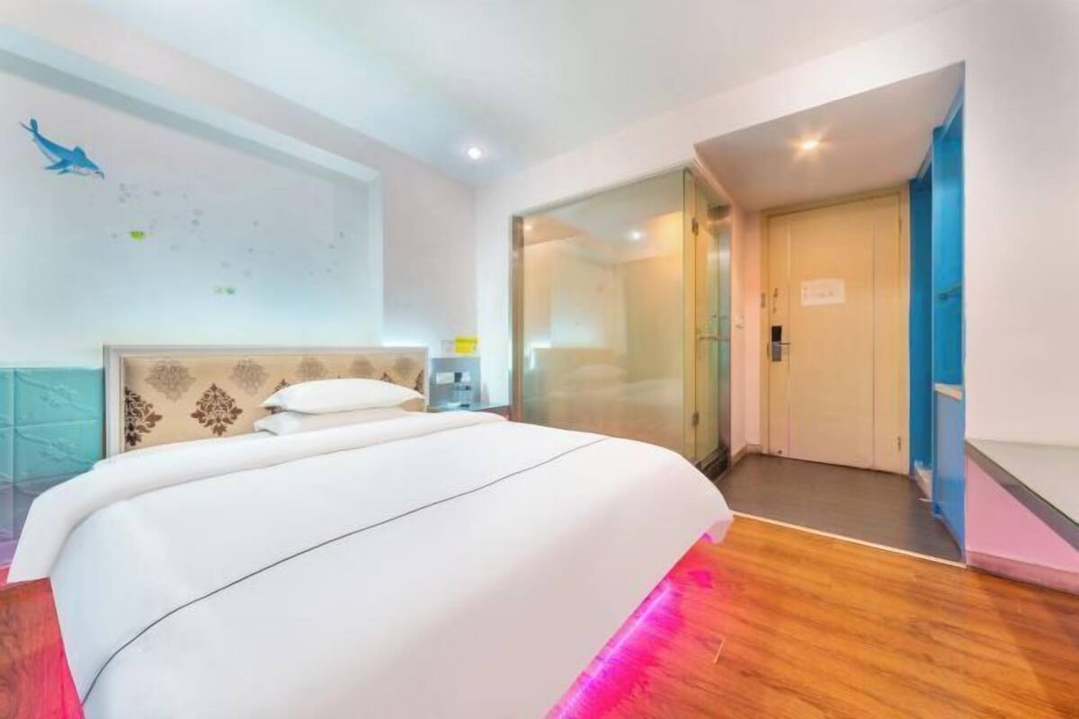 Een hotelkamer met een groot bed, een glazen deur naar een badkamer en een wand met een decoratief patroon.