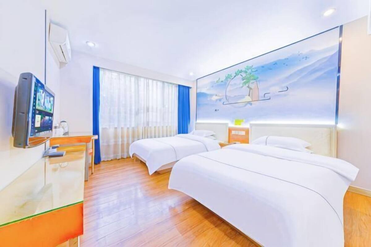 Een hotelkamer met twee bedden, een bureau, een televisie en een groot raam met gordijnen.