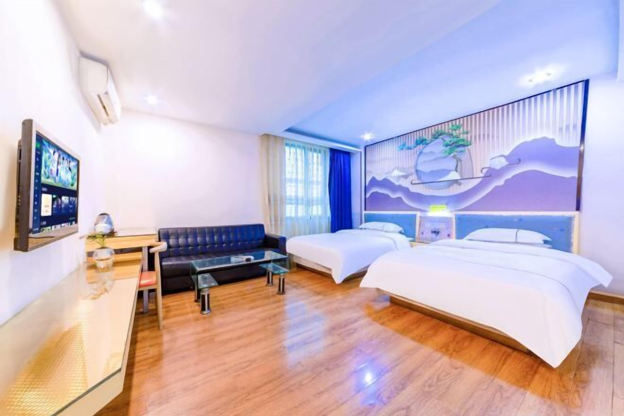 A hotel room with a wooden floor, a sofa, two beds, a TV, and a painting on the wall.
