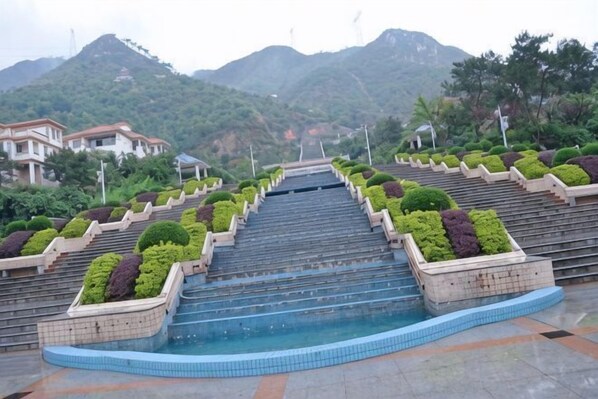 Un escalier mène à une piscine dont les marches sont bordées de jardinières, le tout étant entouré de bâtiments et de collines.