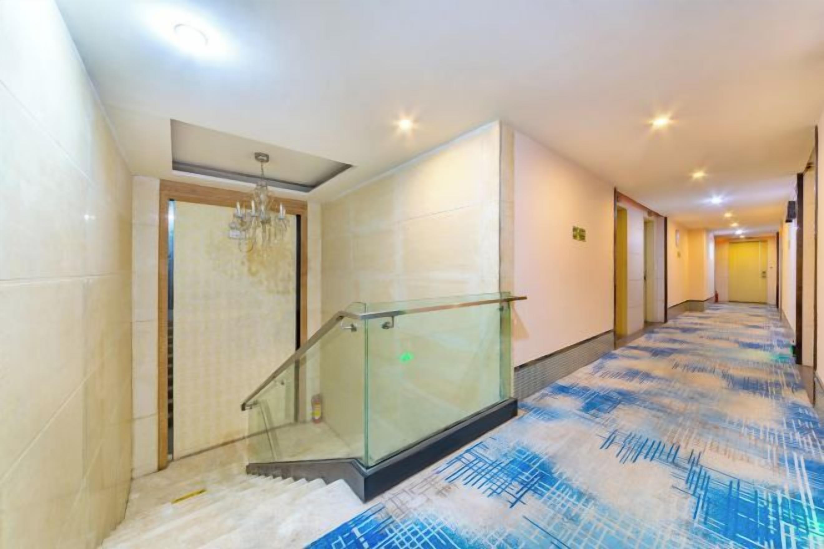 A hotel hallway with a glass railing, a patterned carpet, and a chandelier.