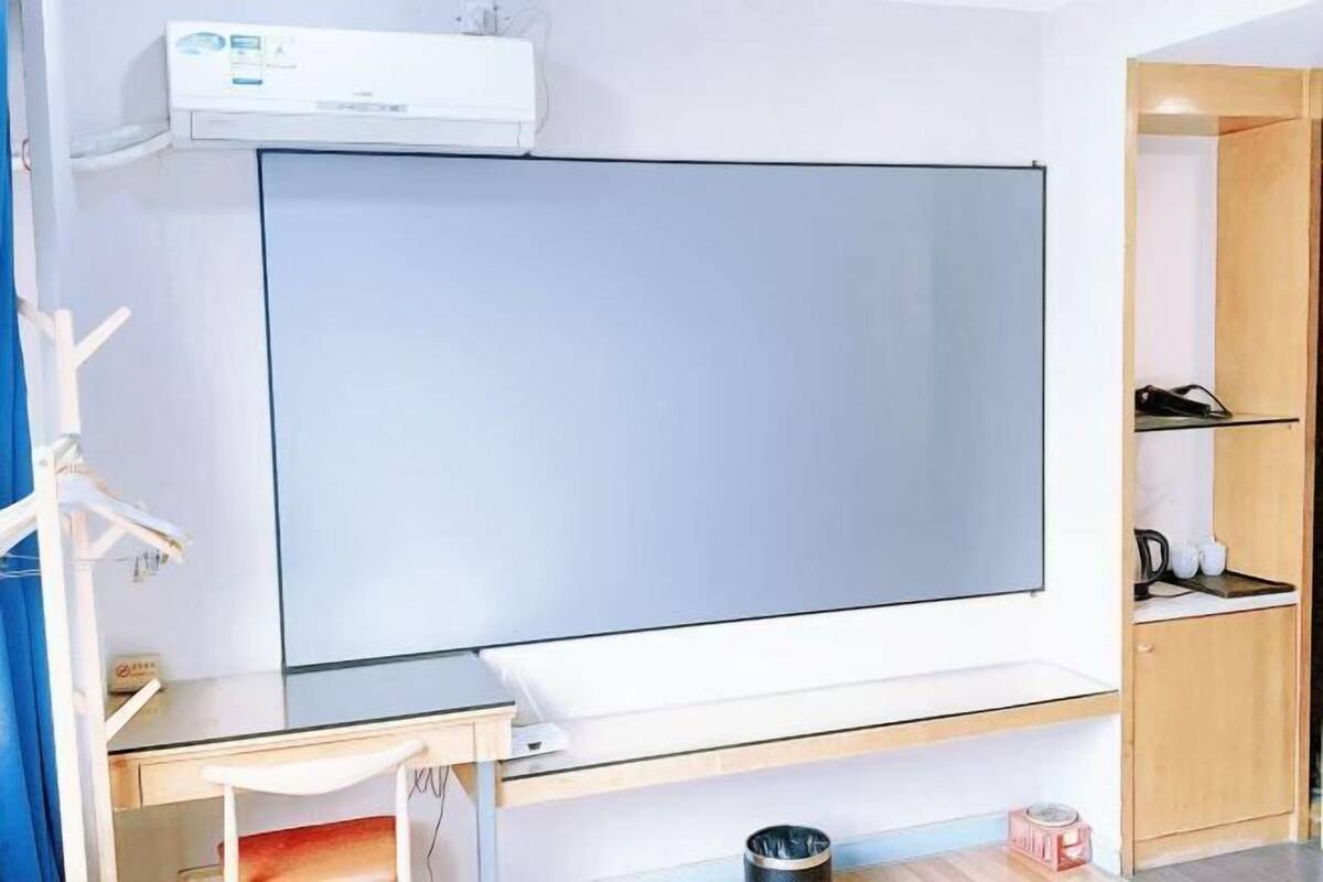 Hotelkamer met een groot flatscreen televisietoestel, een bureau, een stoel, een kleine prullenbak en een houten kast met een plank.