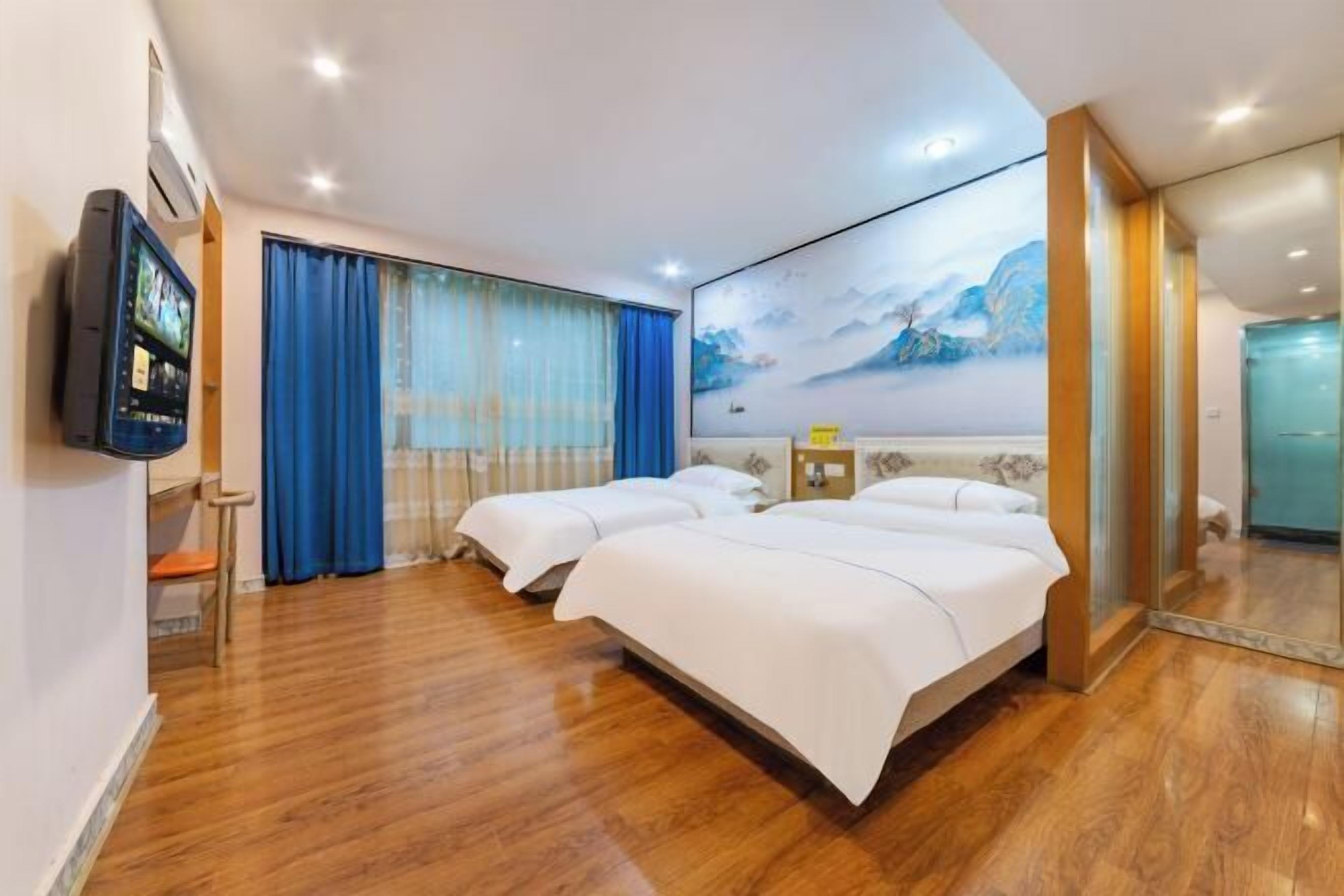 A hotel room with two beds, a TV, a painting, and a wooden floor.