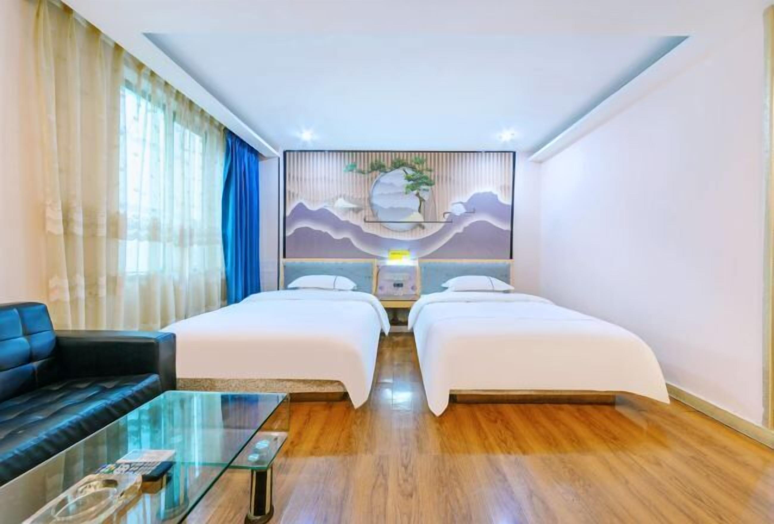 A hotel room with two beds, a sofa, a glass coffee table, and a wall-mounted artwork.