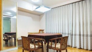 Een eetruimte met een ronde tafel, vier stoelen, een spiegel en een groot raam met gordijnen.