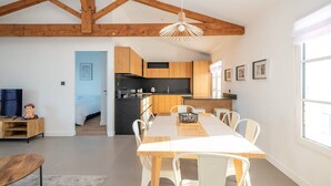 A modern kitchen with wooden beams, a dining area with a table and chairs, and a TV in the living room.