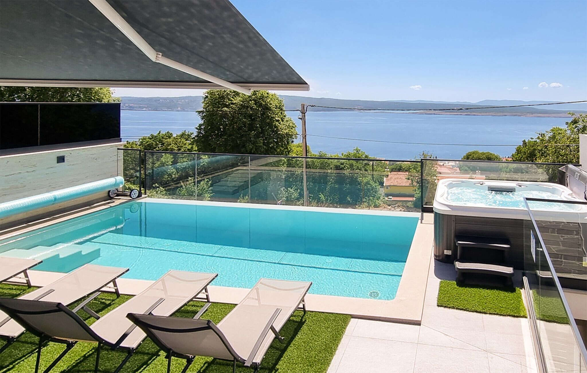 Una piscina con lettini e vasca idromassaggio, con vista su un lago e delle colline.