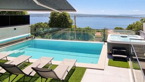 Une piscine dotée de chaises longues et d’un jacuzzi, offrant une vue sur un plan d’eau et des collines.