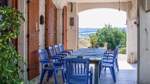 Ein Essbereich im Freien mit einem langen Tisch und blauen Stühlen, umgeben von Holztüren und Blick ins Grüne.