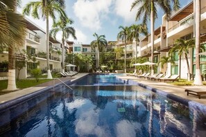 Une piscine entourée de palmiers et de chaises longues, avec un immeuble à plusieurs étages en arrière-plan.