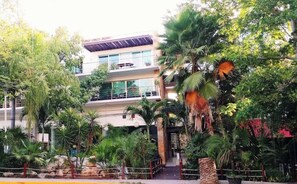 Un immeuble à plusieurs étages doté de balcons, entouré d’une végétation tropicale.