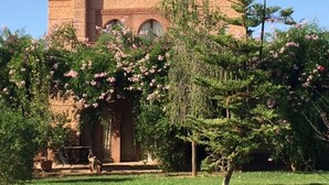 A building with a brick facade, arched windows, and a chimney. There is a tree with pink flowers in the foreground. - Small charming villa (Tamesluht)