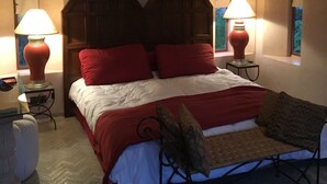 A bedroom with a wooden headboard, two bedside lamps, a bed with red and white bedding, a small table with a lamp, and a window with a view. - Small charming villa (Tamesluht)