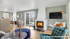 A modern living room with a fireplace, a dining area, and a TV mounted on the wall. - 4 bedroom lovely home in Vejby (Vejby)