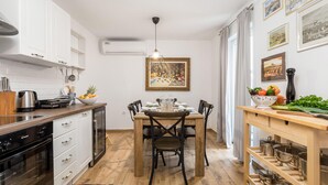A compact kitchen with modern appliances, a dining area with a wooden table and chairs, and a wall-mounted air conditioner. - 2 bedroom amazing apartment in Matulji (Matulji)