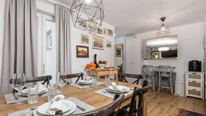 A dining area with a wooden table set for four, surrounded by chairs. There are framed pictures on the wall, a ceiling light fixture, and a coffee machine on a cabinet. - 2 bedroom amazing apartment in Matulji (Matulji)
