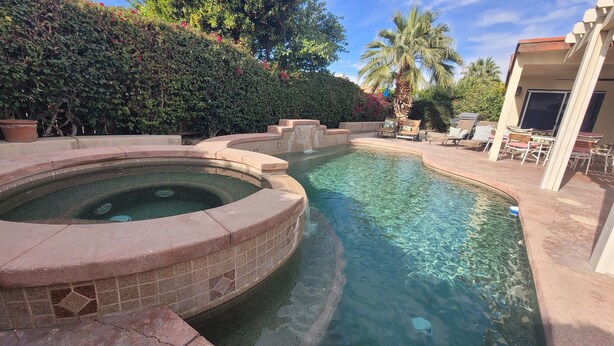 A swimming pool with a hot tub, surrounded by lounge chairs and a landscaped garden.