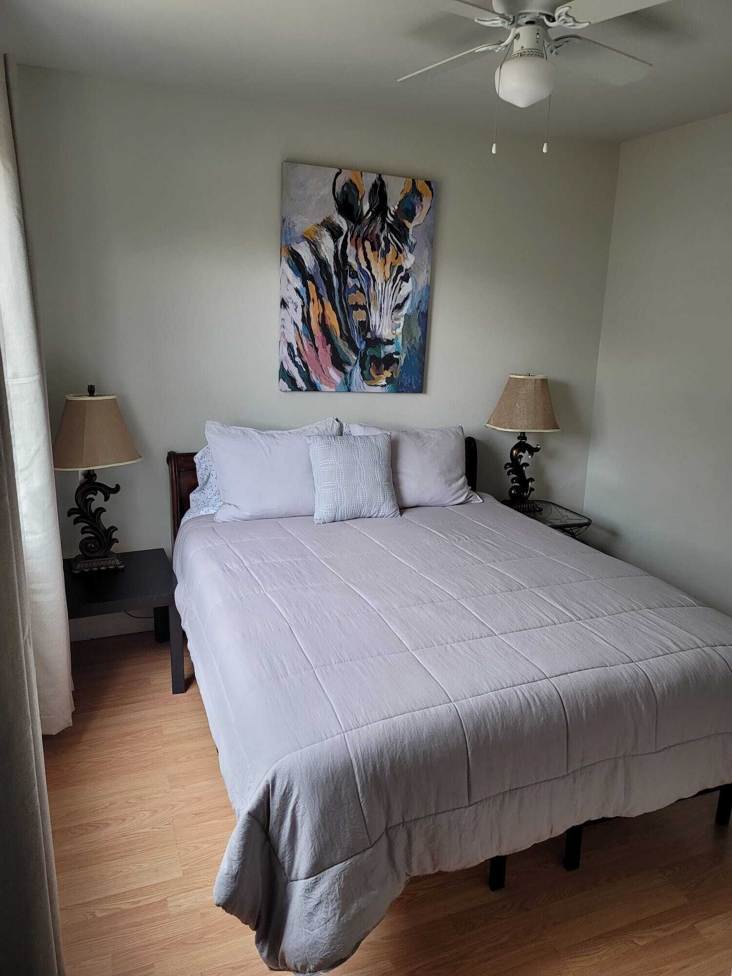 A bedroom with a large bed, two bedside tables with lamps, a ceiling fan, and a painting of a tiger on the wall.