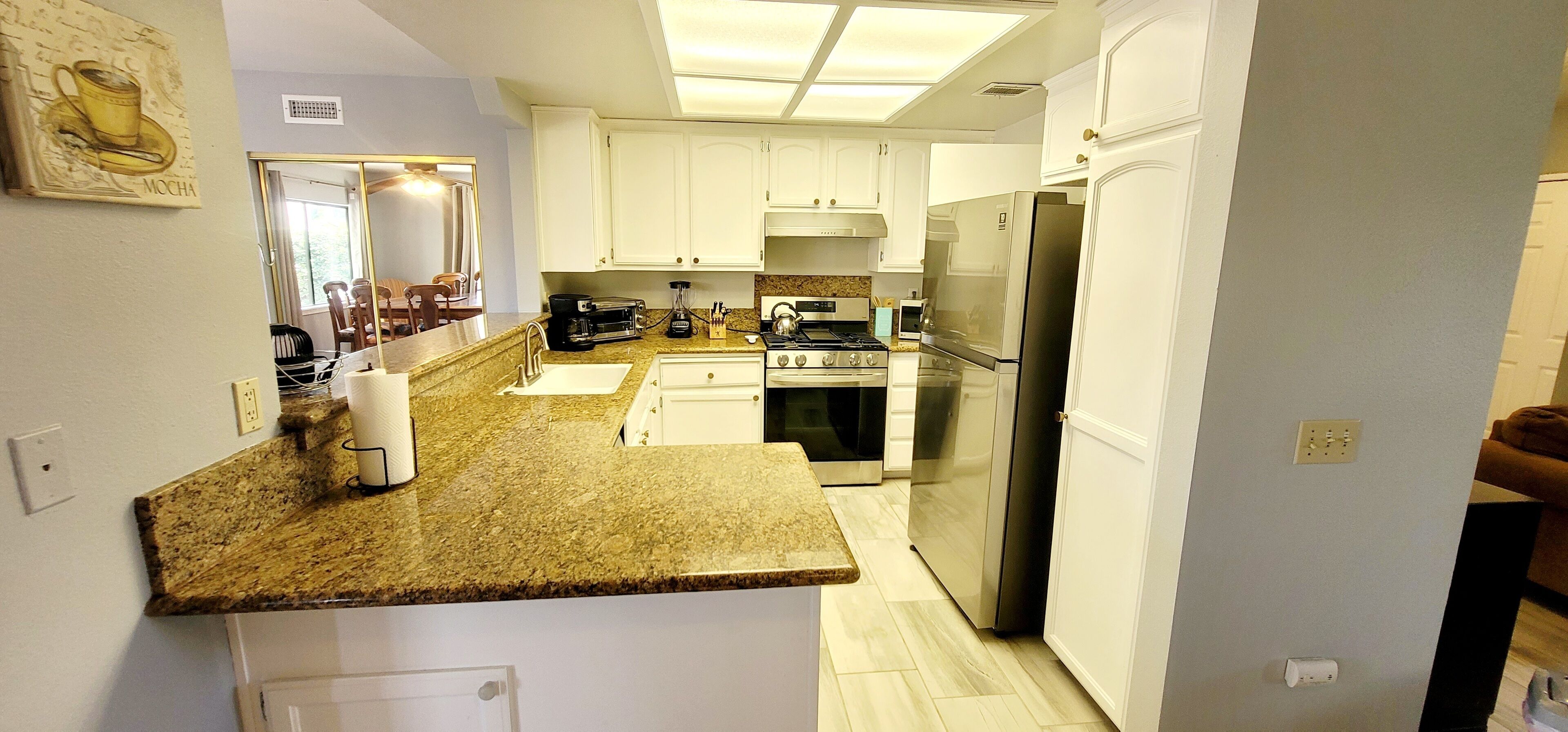 A modern kitchen with white cabinets, granite countertops, stainless steel appliances, and a coffee maker.