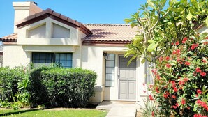 A residential house with a tiled roof, a front door, and a well-maintained garden with bushes and flowering plants.
