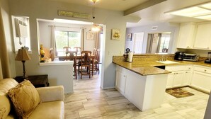 A modern kitchen with white cabinets, a granite countertop, and a dining area with wooden chairs.