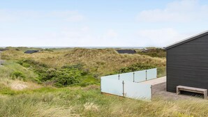 Un edificio costiero con facciata scura, immerso in dune erbose e affacciato su un mare limpido.