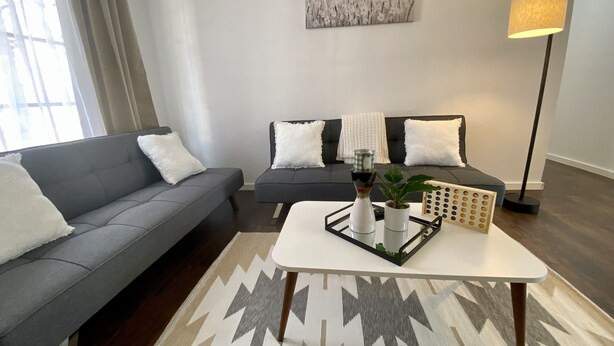 Un salon moderne avec un canapé gris, une table basse agrémentée d’objets décoratifs, un lampadaire et un tapis à motifs.