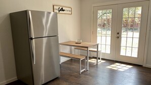 Une cuisine équipée d’un réfrigérateur en acier inoxydable, d’une table en bois avec un banc, et d’une porte dotée d’une fenêtre.