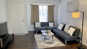Un salon moderne avec un parquet en bois foncé, un ensemble de canapés gris, une table basse blanche et un ventilateur de plafond.