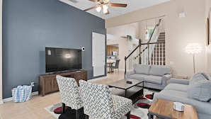 A modern living room with a flat-screen TV, patterned chairs, a coffee table, and a staircase leading to an upper level.