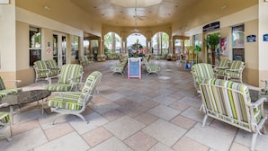 A covered outdoor seating area with striped chairs and a central table, surrounded by arches and potted plants.