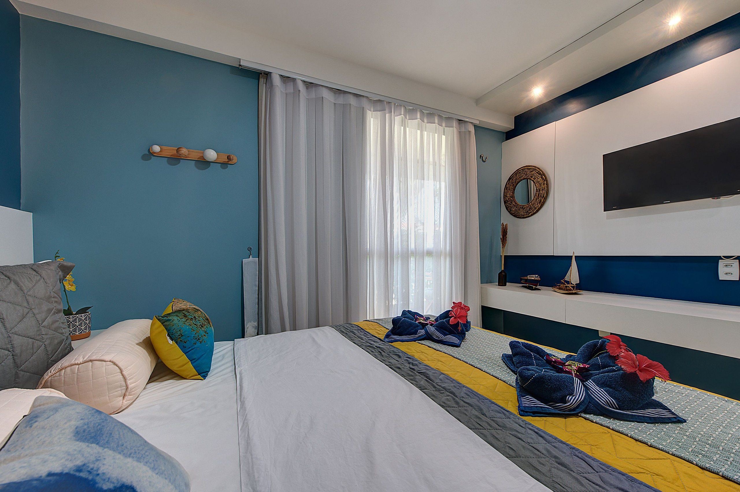 Una habitación de hotel con cama, televisión, un pequeño estante con adornos y una ventana con cortinas.