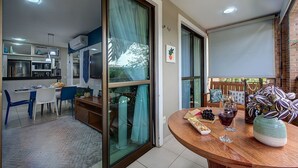 A modern kitchen with a dining area, a sliding glass door leading to a balcony, and a wooden table with wine glasses and snacks. - Apart em Porto das Dunas por Carpediem (Aquiraz)