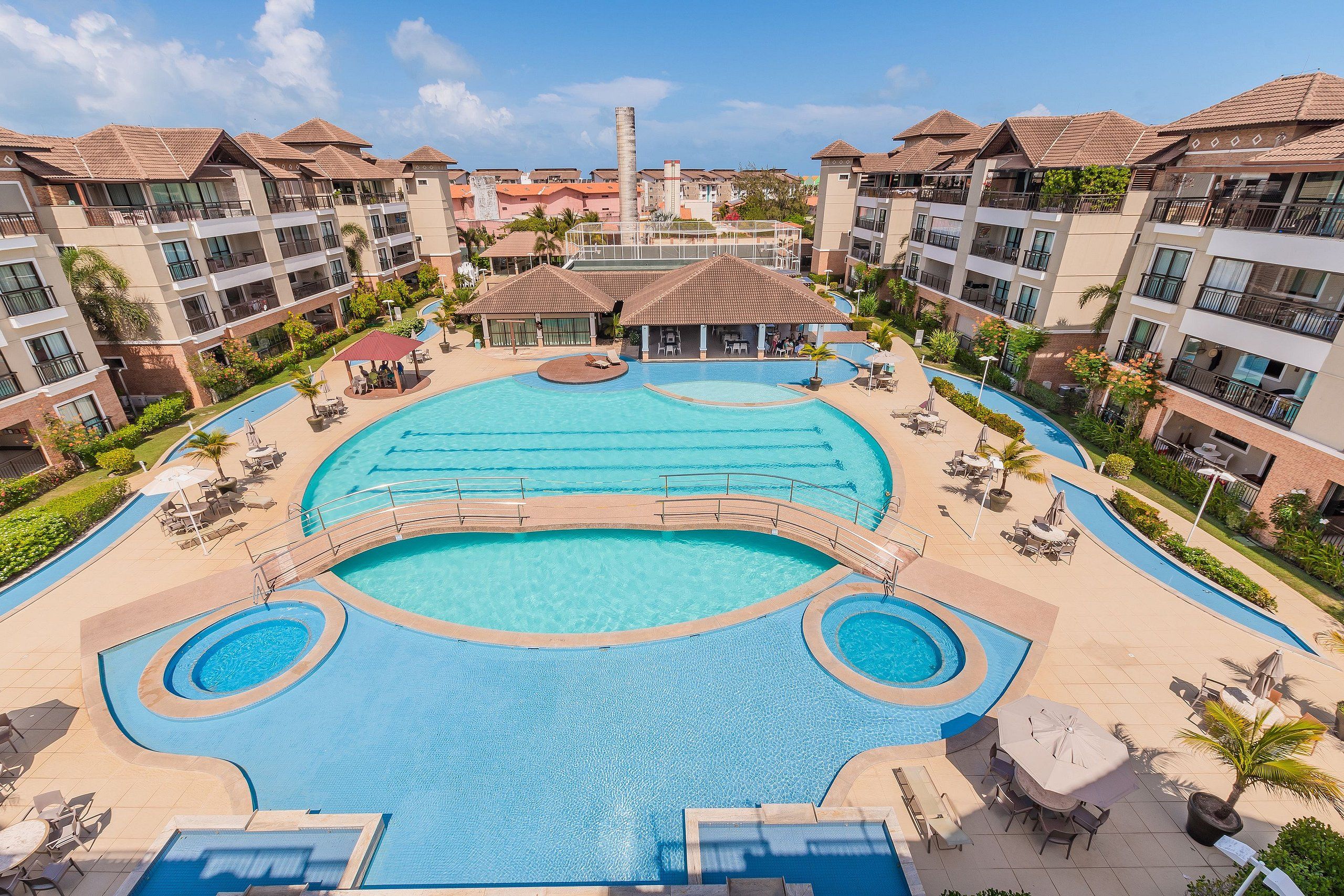 Un resort con una amplia piscina central, varios balcones y zonas de estar al aire libre.