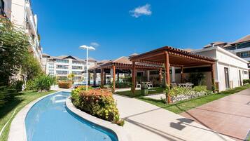 Edifício residencial com piscina, área de estar ao ar livre e céu azul límpido.