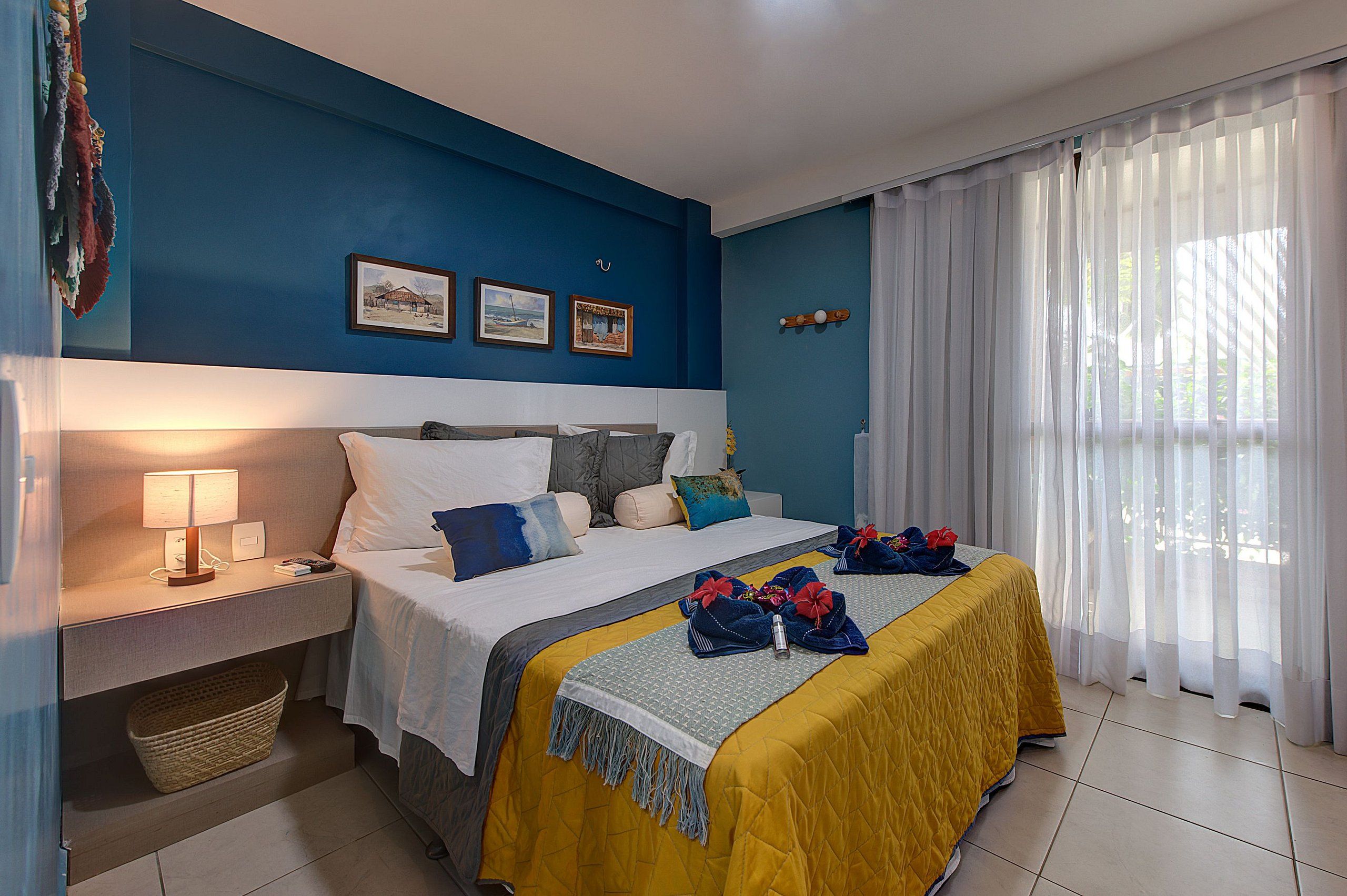 Quarto de hotel com cama, mesa de cabeceira, luminária e obra de arte na parede.