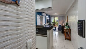 A modern kitchen with a built-in island, a wall-mounted air conditioner, and a digital keypad lock. - Apart em Porto das Dunas por Carpediem (Aquiraz)
