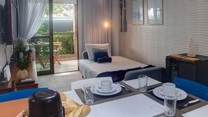 A hotel room with a bed, a dining area with a table set for two, a desk with a computer, and a view of the outdoors. - Apart em Porto das Dunas por Carpediem (Aquiraz)