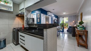 A modern kitchen with a central island, built-in appliances, and a dining area with a view of the outdoors. - Apart em Porto das Dunas por Carpediem (Aquiraz)