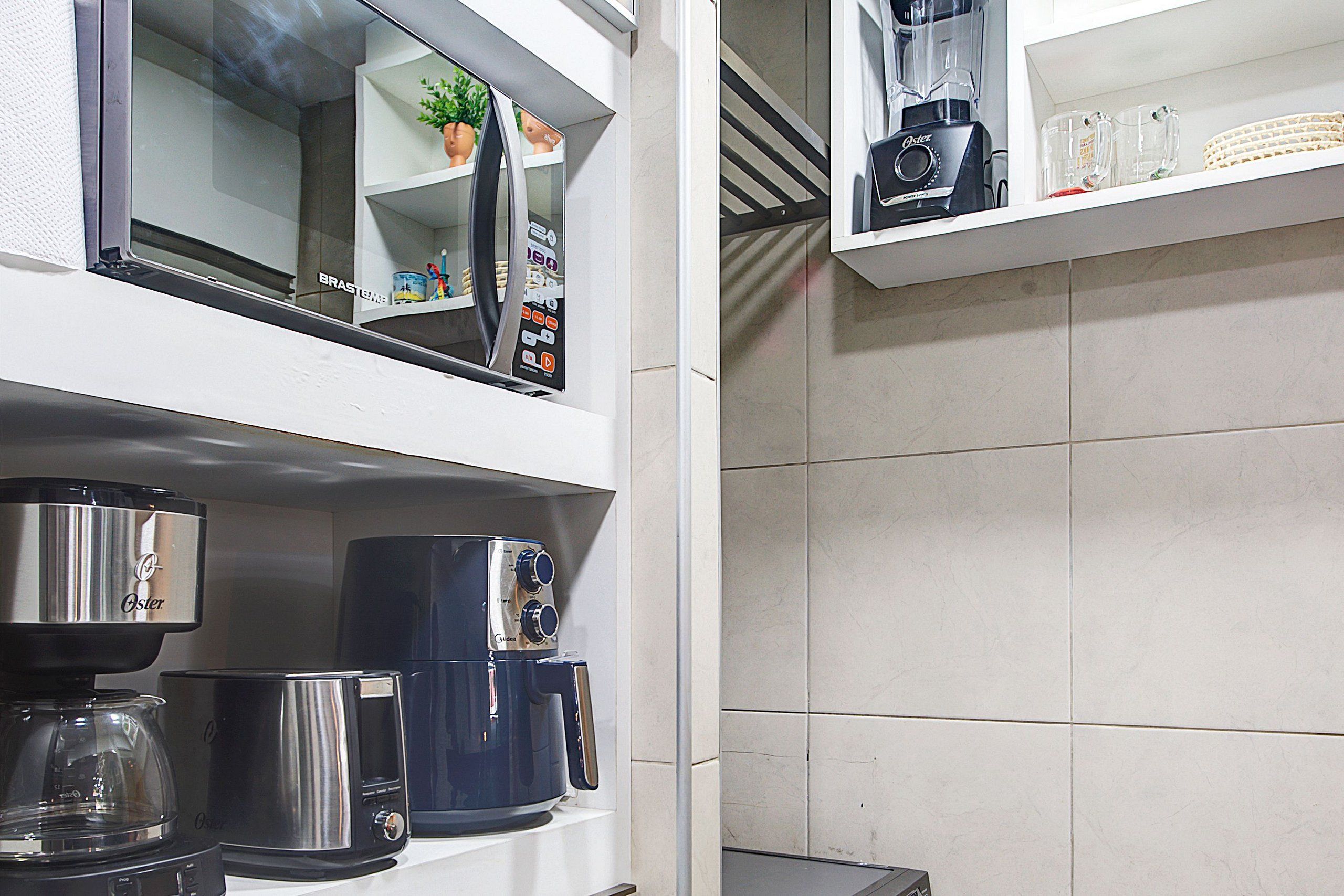 Una cocina con cafetera, licuadora y estante con una planta y un vaso.