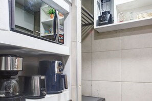 Een keuken met een koffiezetapparaat, een blender en een plankje met een plant en een glas.