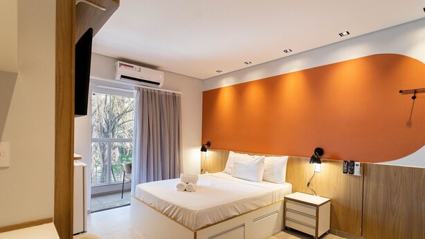 Una habitación de hotel moderna con una cama grande, mesitas de noche, un escritorio y vistas al exterior.