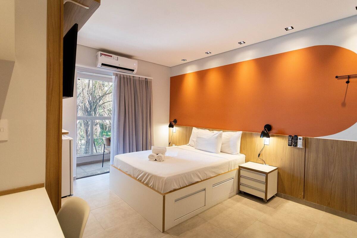 Une chambre d’hôtel moderne, dotée d’un grand lit, de tables de chevet, d’un bureau et offrant une vue sur l’extérieur.