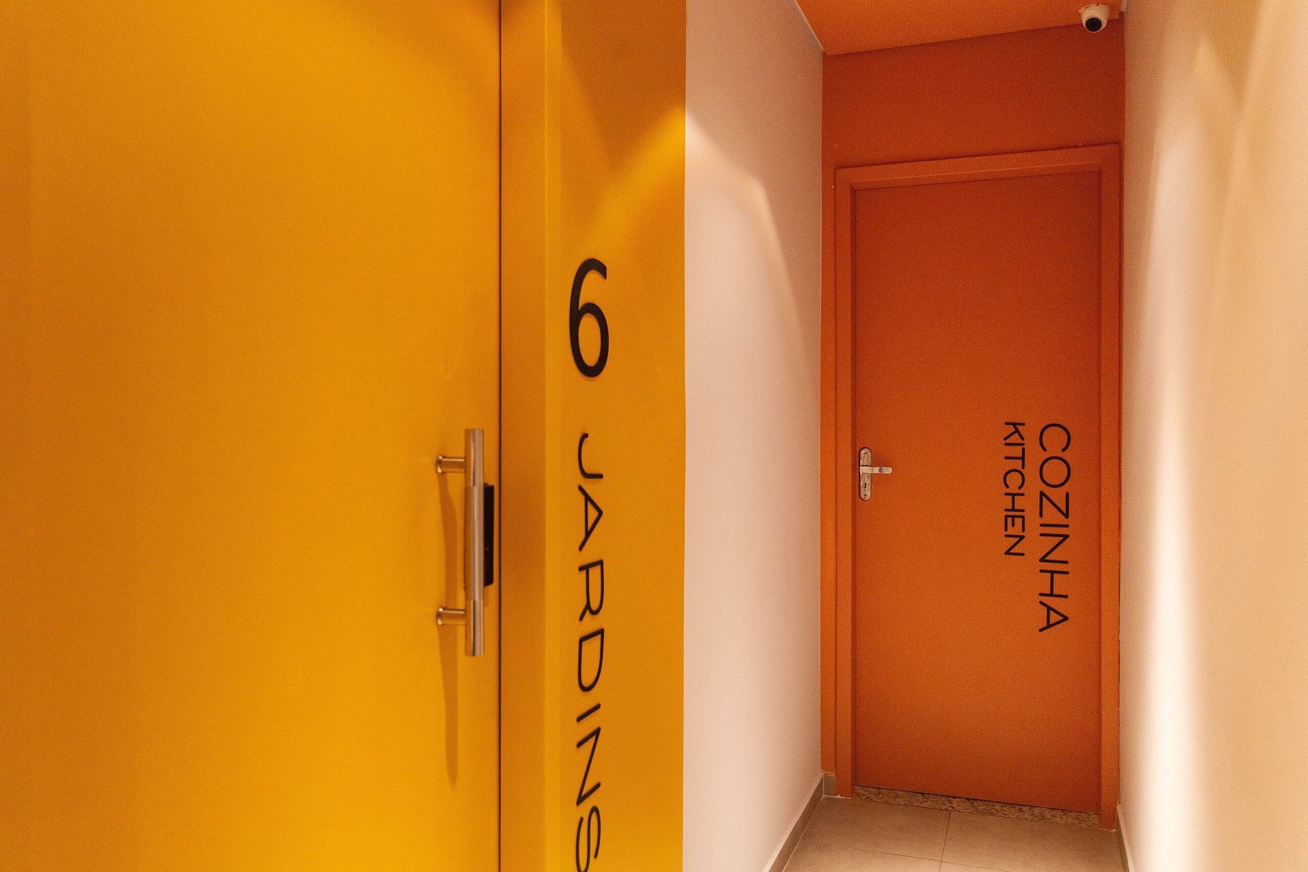 A hallway with doors labeled "6 JARDINS" and "COZINHA KITCHEN".